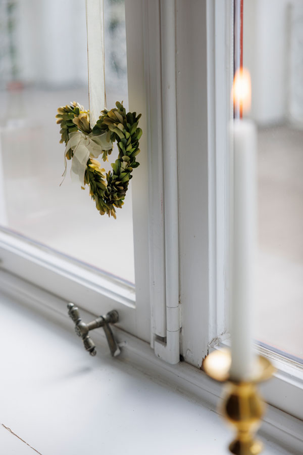 ein Ornament aus Buchszweigen mit einer Kerze vor einem alten Fenster